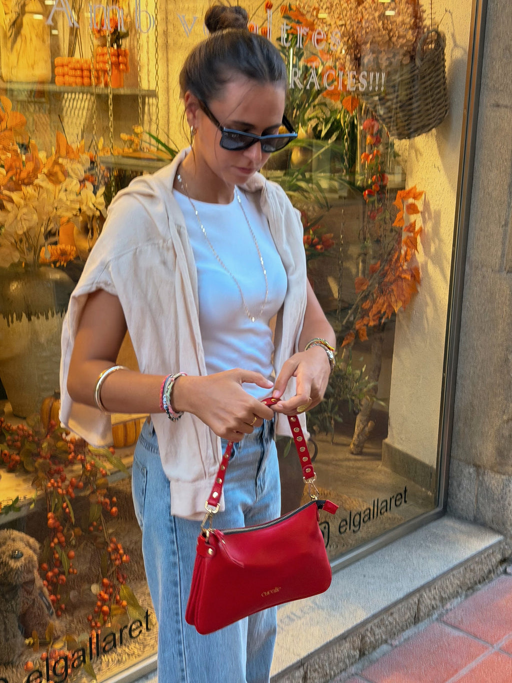 Bolso Colin mini de piel roja en la mano, frente a un escaparate de Vic — Cucolie