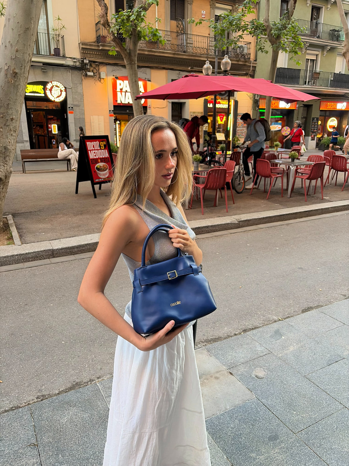 Bolso Cuco mini de piel azul marino, con su hebilla, frente a una terraza — Cucolie