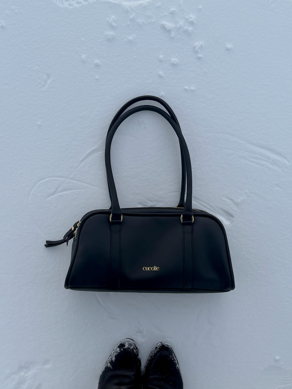 Bolso Cucolie de piel negra con dos asas, sobre la nieve