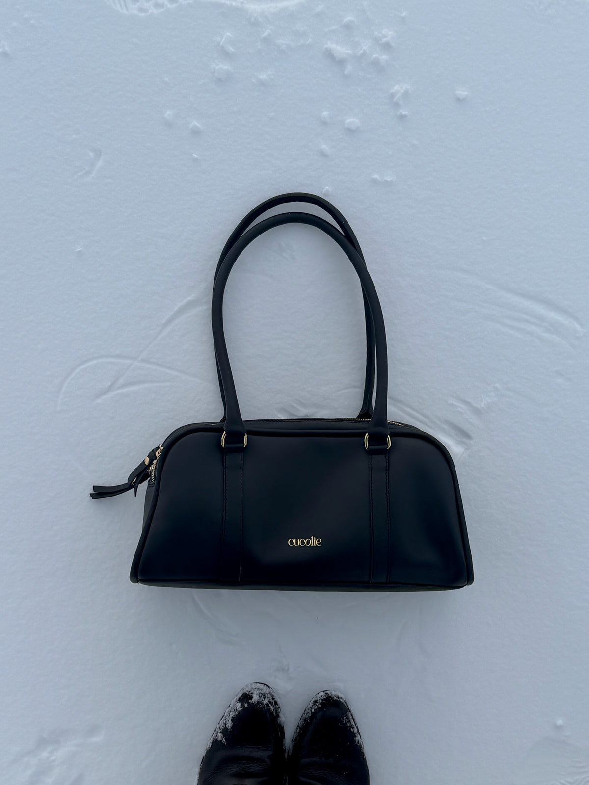 Bolso Cucolie de piel negra con dos asas, sobre la nieve