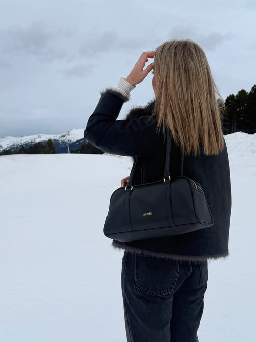 Bolso Cucolie de piel negra llevado al hombro en la nieve