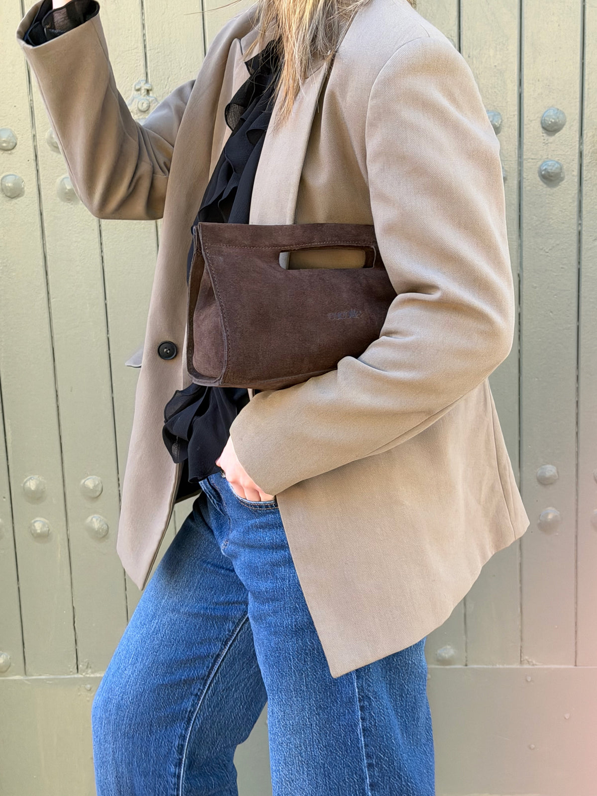Bolso Cucolie de serraje marrón bajo el brazo, frente a una puerta verde